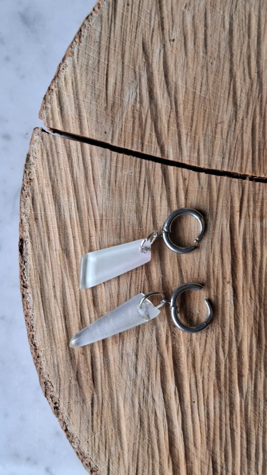 Boucles d'oreilles en verre recyclé blanc laiteux posées à plat sur un support en bois