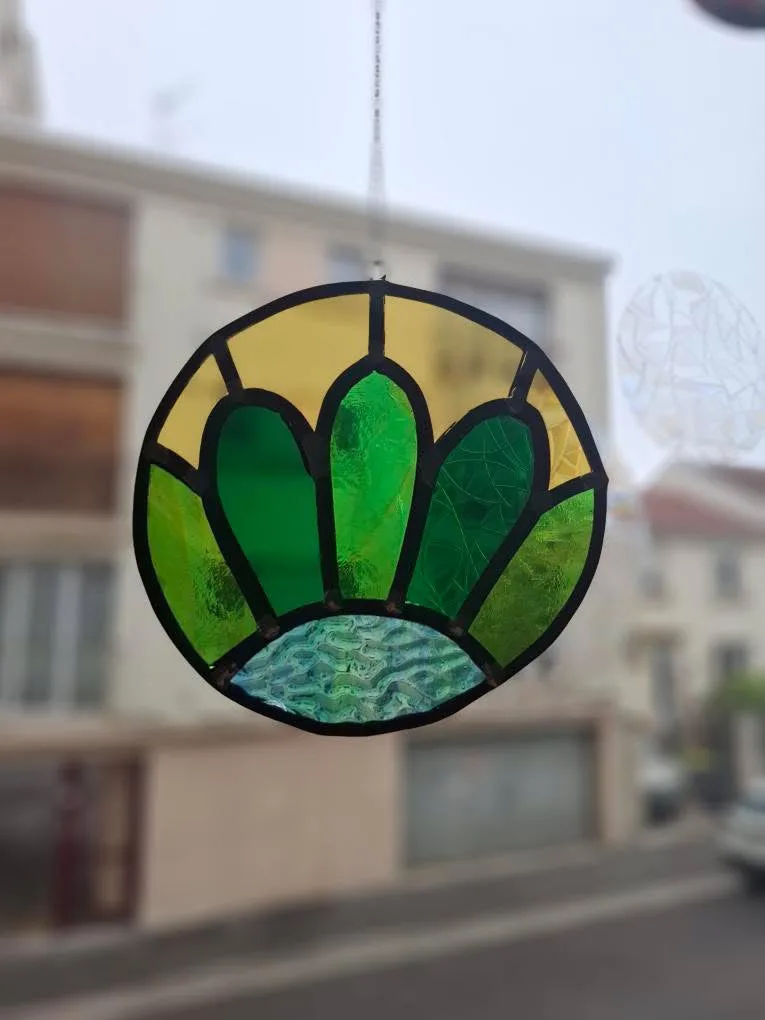 Vitrail rond suspendu par une chaînette, à motif floral stylisé vert, jaune et bleu texturé