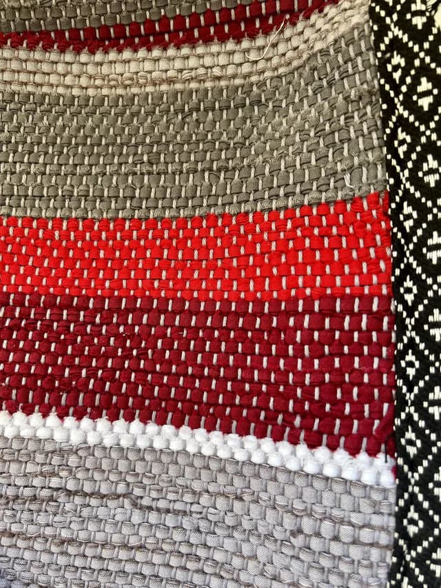 Gros plan sur le tissage texturé aux rayures rouges, bordeaux et grises avec galon