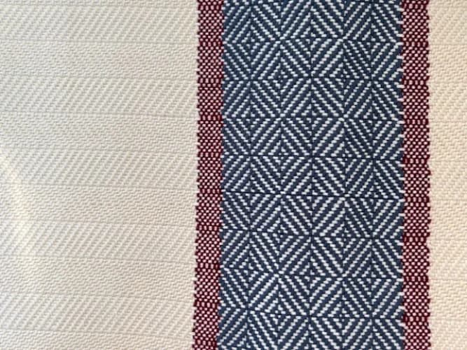 Gros plan sur le tissage chevron beige et la bande ornée de motifs géométriques bleus et rouges.