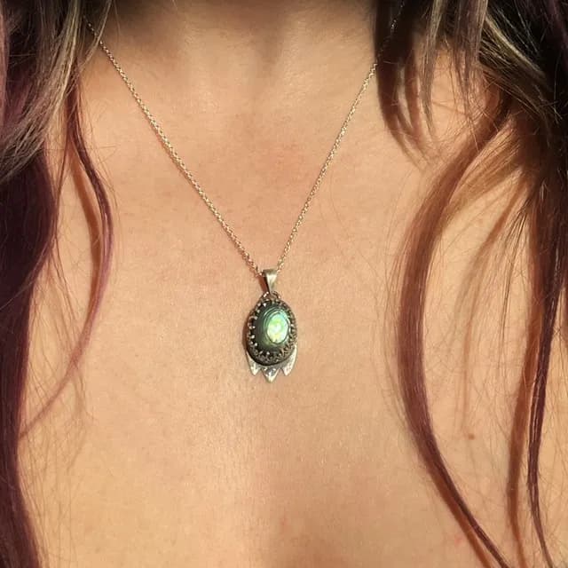 Pendentif Exspiravit en argent et abalone aux reflets verts porté sur un décolleté.