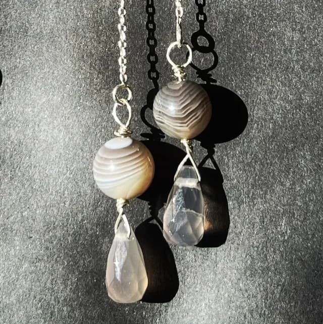Chaînettes d'oreilles en argent avec perles rondes et gouttes d'agate facettées sur fond gris.