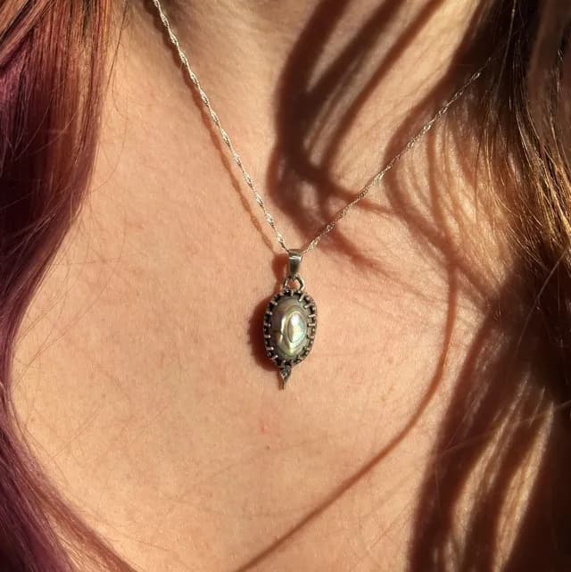 Pendentif Nox avec cabochon nacré porté au cou, baigné de lumière naturelle.