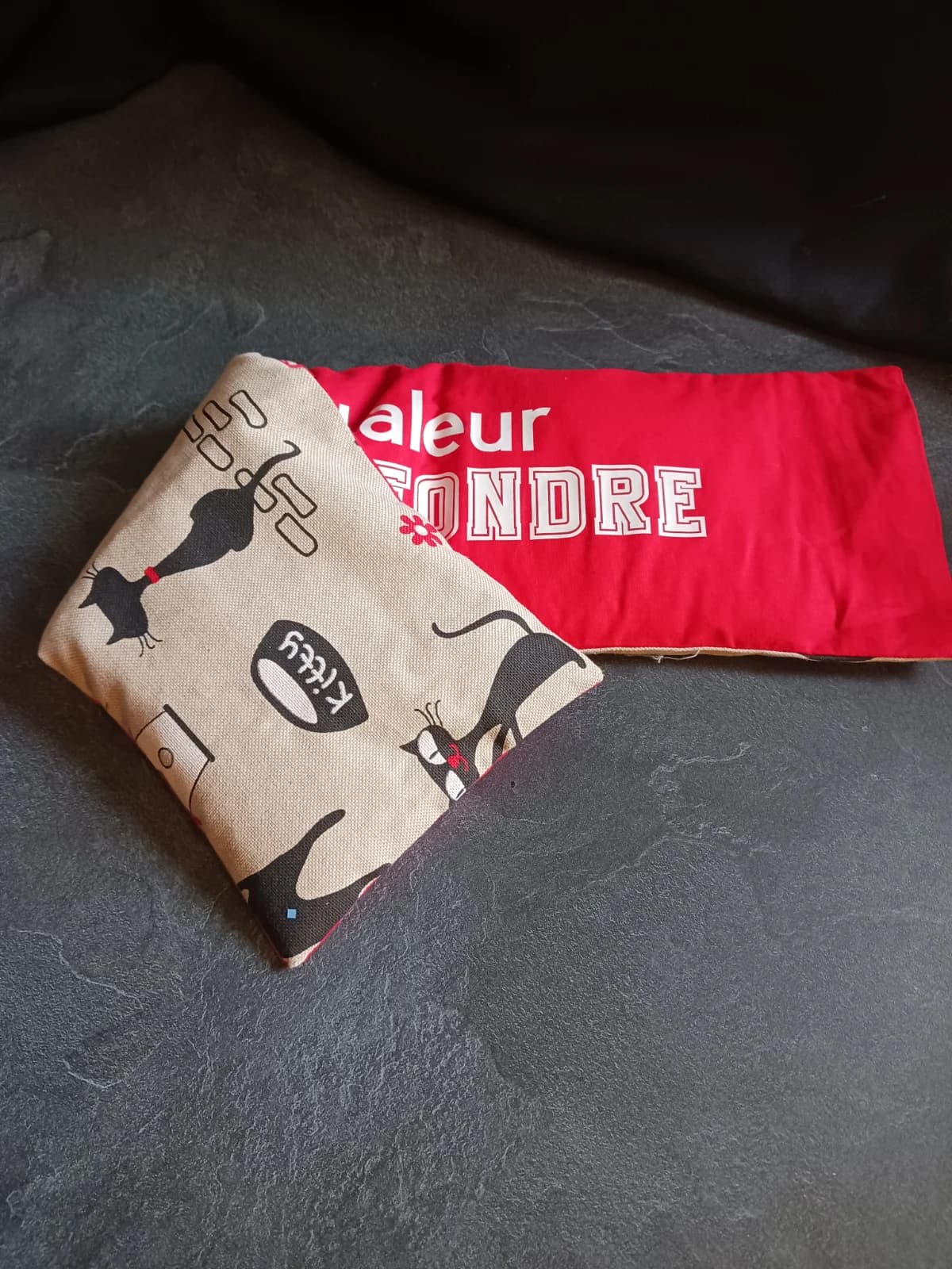 Bouillotte rouge repliée laissant apparaître le dos en tissu beige à motifs de chats