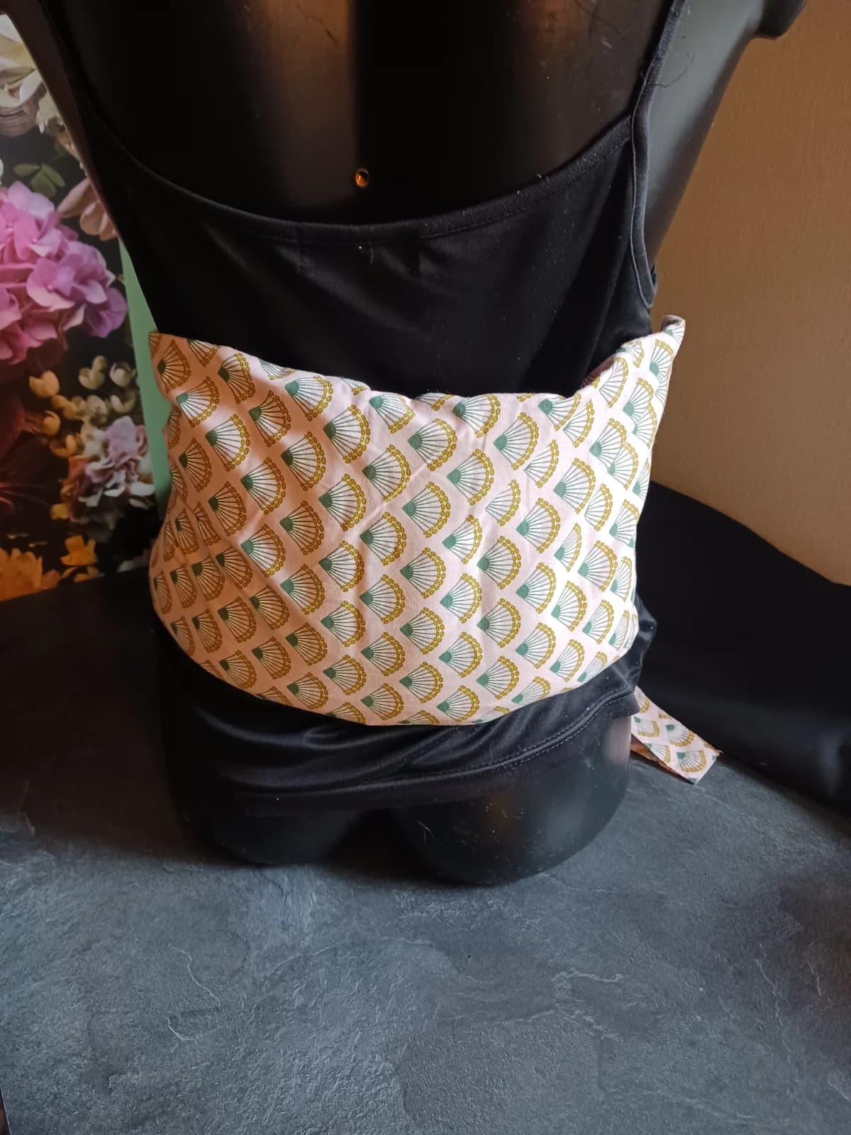 Vue arrière d'un buste portant la bouillotte lombaire en tissu rose à motifs d'éventails verts et dorés.